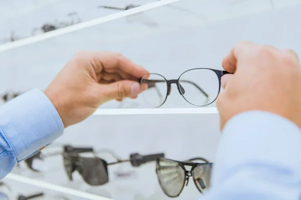Vista cortada da pessoa que toma óculos da prateleira na óptica — Fotografia de Stock