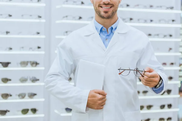 Обрізаний вид окуляра в білому пальто, що тримає окуляри та цифровий планшет в оптиці — Stock Photo