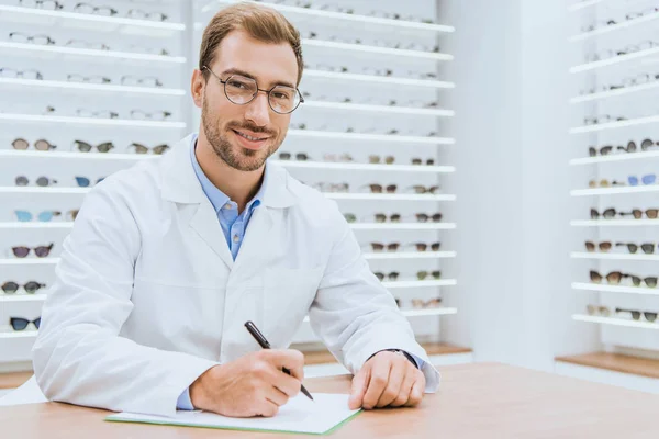 Профессиональный оптометрист, пишущий диагноз в офтальмологическом магазине — стоковое фото