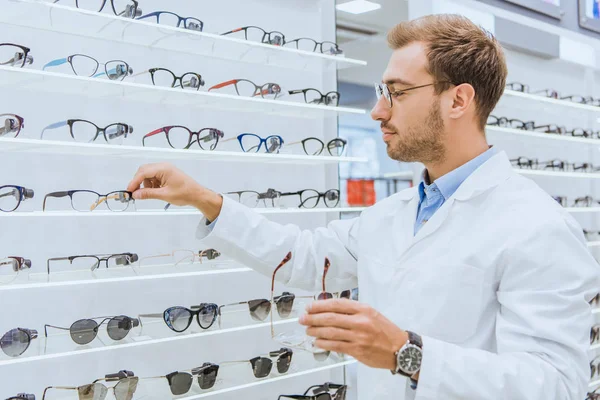 Professional oculist taking eyeglasses from shelves in ophthalmic shop — Stock Photo