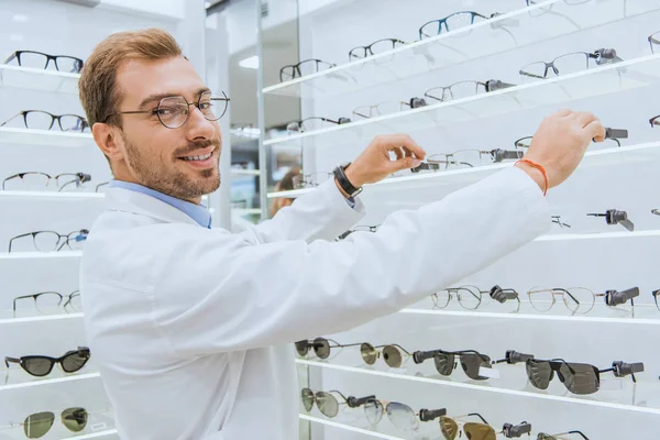Smiling optician taking eyesight from shelves in ophthalmic shop — Stock Photo