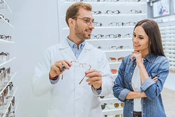 Male optometrist showing eyeglasses to smiling woman in optica — Stock Photo