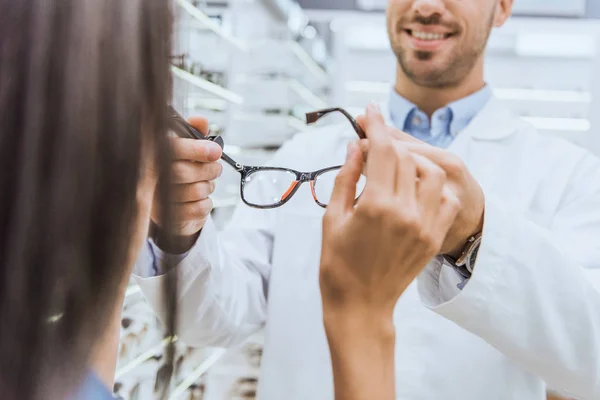 Partial view of male oculist giving eyeglasses to woman in ophthalmic shop — Stock Photo