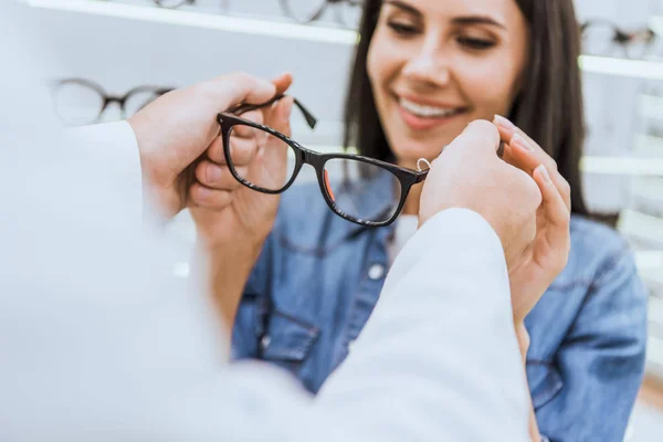 Imagen recortada de oculista masculino dando gafas a la mujer en óptica - foto de stock
