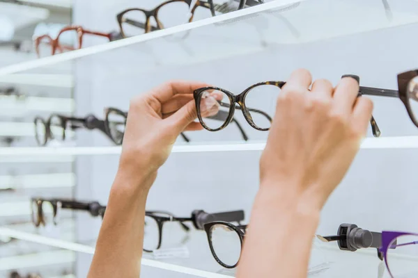 Partial view of optician taking glasses from shelf in ophthalmic shop — Stock Photo