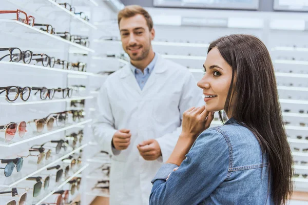 Messa a fuoco selettiva della donna sorridente in piedi vicino con l'oculista maschio nel negozio oftalmico — Foto stock