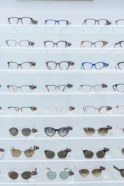 Estantes con gafas elegantes y gafas de sol de moda en la tienda oftálmica - foto de stock