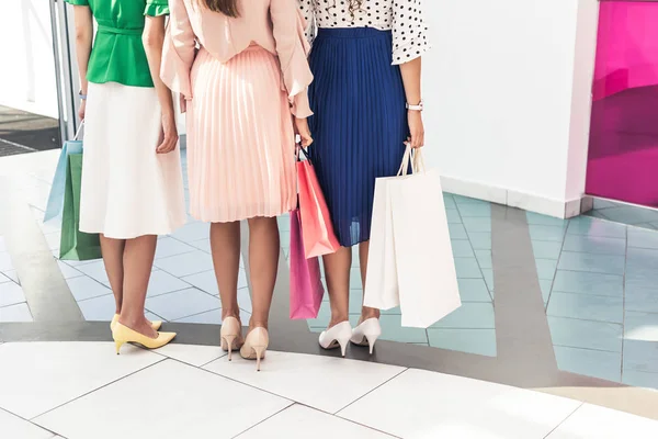 Низкая группа молодых женщин, держащих бумажные пакеты и стоящих вместе в торговом центре — стоковое фото