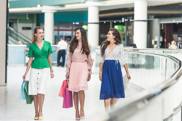 Beautiful smiling young women holding shopping bags and walking together in mall — Stock Photo