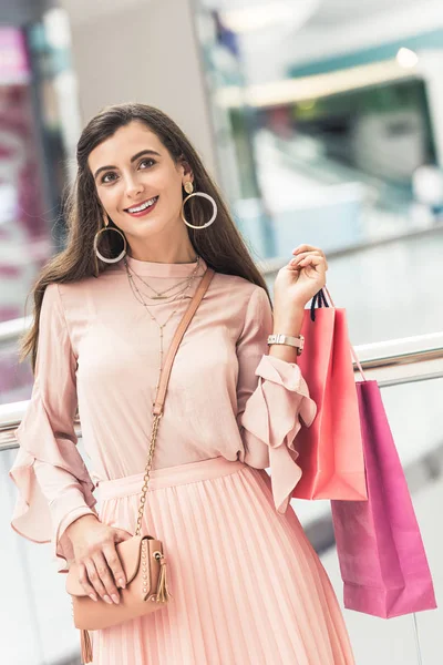 Hermosa mujer joven sonriente sosteniendo bolsas de papel en el centro comercial - foto de stock