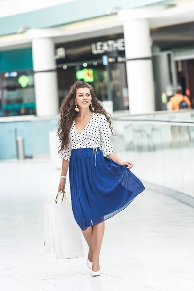 Beautiful smiling young woman holding paper bags and walking in shopping mall — Stock Photo