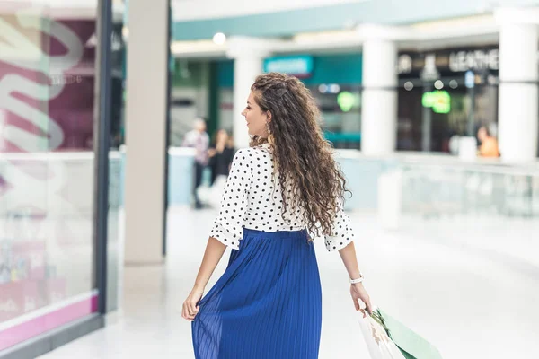 Visão traseira da jovem mulher feliz com sacos de papel andando no shopping — Fotografia de Stock
