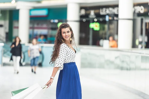 Красива стильна молода жінка тримає сумки і посміхається на камеру в торговому центрі — стокове фото