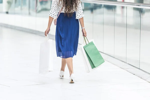 Вид сзади на девочку, держащую бумажные пакеты и идущую по магазину — стоковое фото