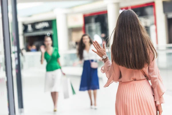 Back view of young woman greeting female friends while walking in shopping mall — Stock Photo