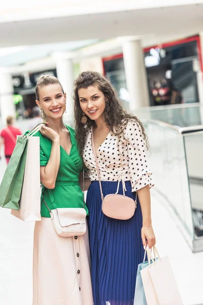 Beautiful stylish young women holding shopping bags and smiling at camera in mall — Stock Photo