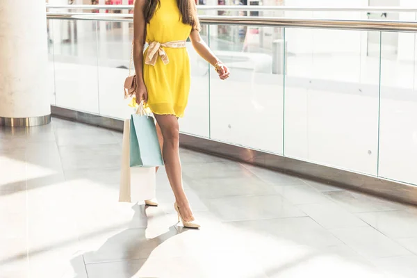 Schnappschuss eines stilvollen Mädchens in gelbem Kleid, das Papiertüten hält und in einem Einkaufszentrum spaziert — Stockfoto
