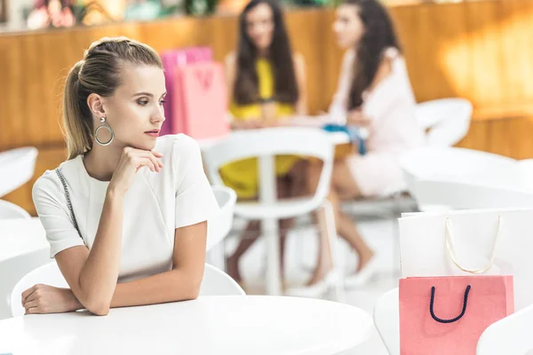 Pensive young woman sitting at table and looking away in cafe at shopping mall — Stock Photo