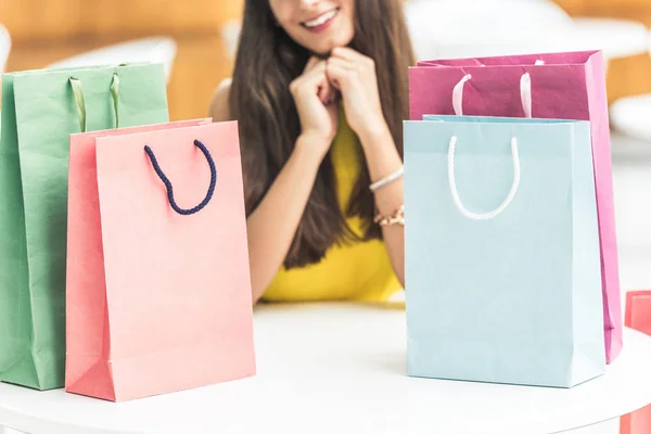 Cropped shot of smiling young woman sitting at table with shopping bags — Stock Photo