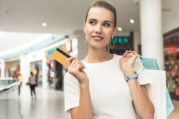Belle jeune femme souriante tenant des sacs en papier et carte de crédit dans le centre commercial — Photo de stock