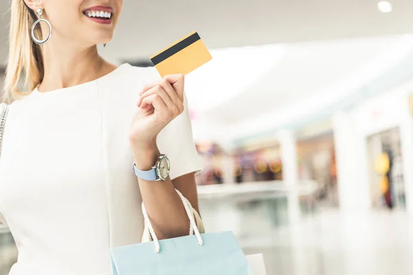 Recortado disparo de sonriente mujer joven sosteniendo tarjeta de crédito en el centro comercial - foto de stock