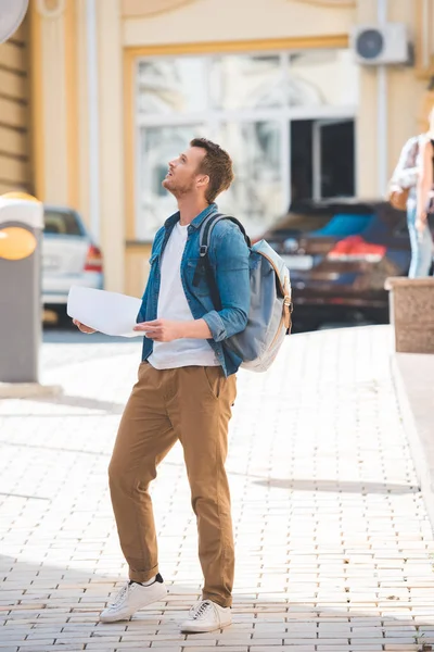 Viajero con mochila y mapa caminando por la calle de la ciudad - foto de stock