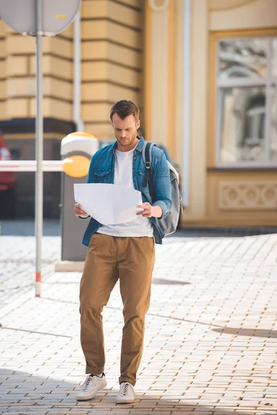 Traveler with backpack looking for destination on map while walking on city street — Stock Photo