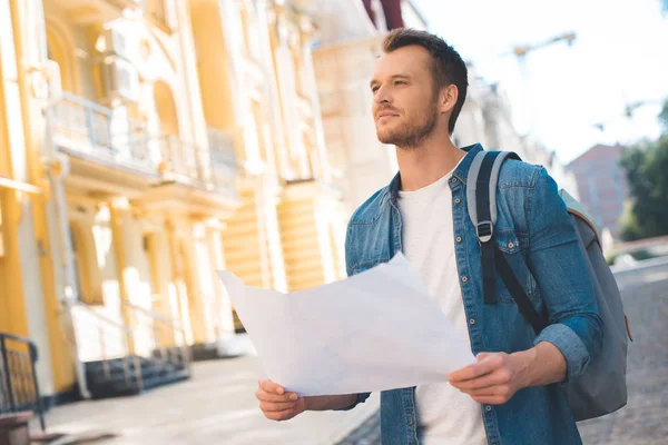 Bellissimo giovane turista con zaino e mappa guardando in alto sulla strada — Foto stock