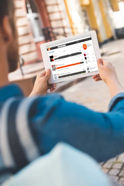 Cropped shot of young man using tablet with soundcloud website on screen while walking by street — Stock Photo