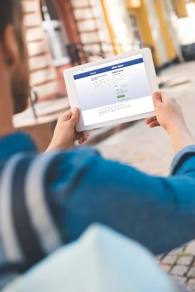 Cropped shot of young man using tablet with facebook website on screen while walking by street — Stock Photo