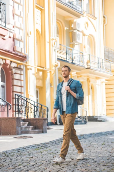 Young traveller with backpack walking by street and looking at camera — Stock Photo