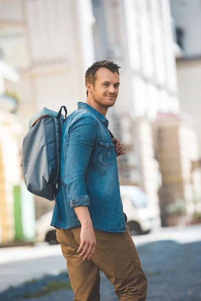 Attractive young tourist with backpack walking by street and looking at camera — Stock Photo