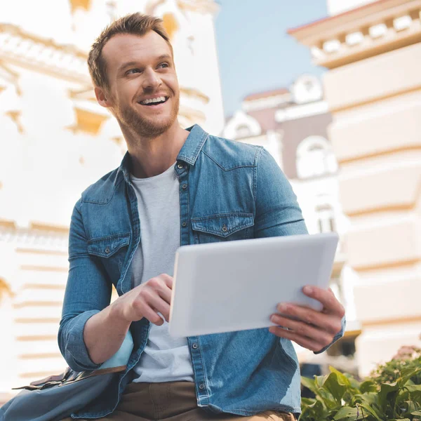 Joven feliz usando la tableta en la calle y mirando hacia otro lado - foto de stock