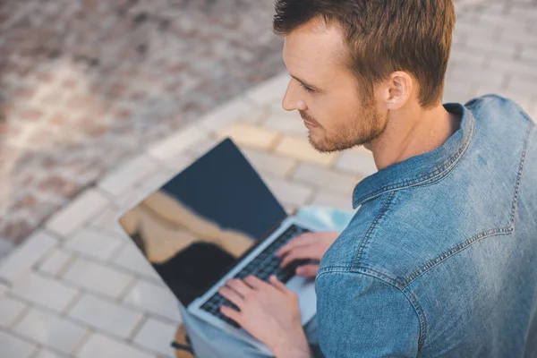 High angle view of handsome young man using laptop with blank screen on street — Stock Photo