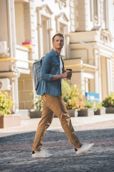 Jovem bonito com café para ir e mochila andando pela cidade — Fotografia de Stock