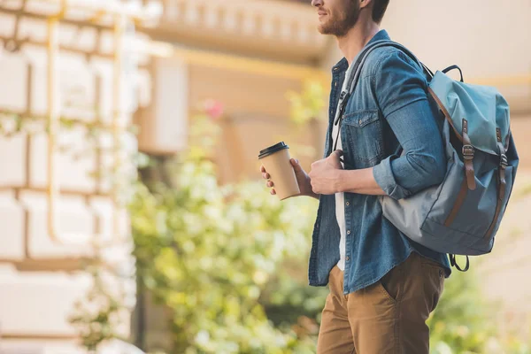 Plan recadré de jeune homme attrayant avec du café pour aller et sac à dos marche par ville — Photo de stock