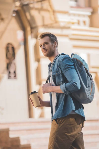 Heureux jeune homme avec café pour aller et sac à dos à pied par la ville — Photo de stock