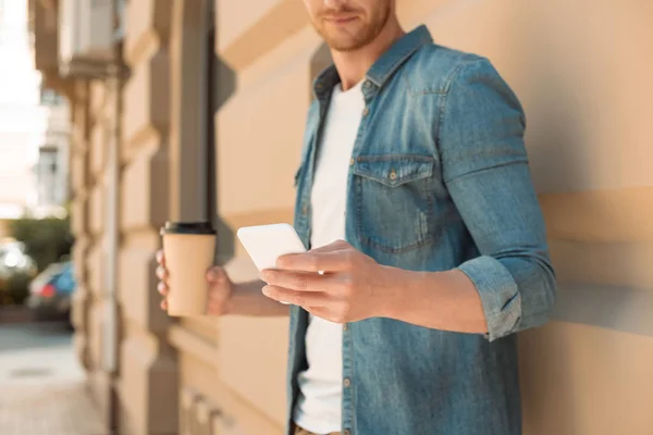 Plan recadré de jeune homme avec du café pour aller à l'aide d'un smartphone dans la rue — Photo de stock