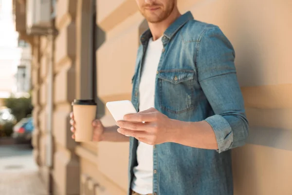 Tiro cortado de jovem com café para ir usando smartphone na rua — Fotografia de Stock