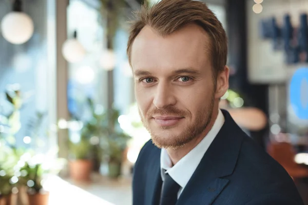 Porträt eines lächelnden Geschäftsmannes im Anzug, der im Café in die Kamera blickt — Stockfoto