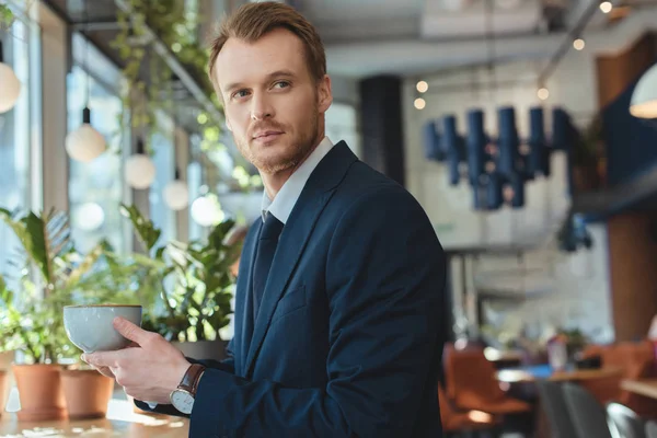 Pensive businessman in suit with cup of coffee having coffee break in cafe — Stock Photo