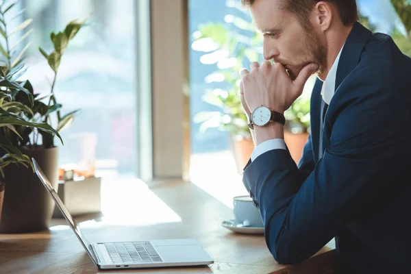 Seitenansicht von nachdenklichen Geschäftsmann Blick auf Laptop-Bildschirm am Tisch mit Tasse Kaffee im Café — Stockfoto