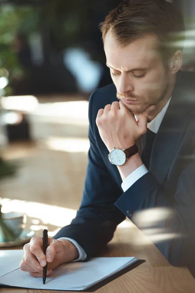 Hombre de negocios centrado haciendo papeleo en la mesa con una taza de café en el restaurante - foto de stock