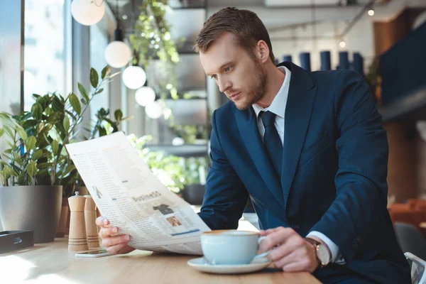 Businessman with cup of coffee reading newspaper during coffee break in cafe — Stock Photo