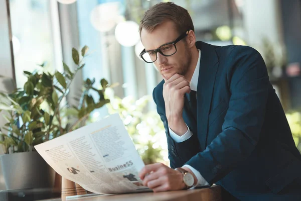 Concentrated businessman in eyeglasses reading newspaper in cafe — Stock Photo