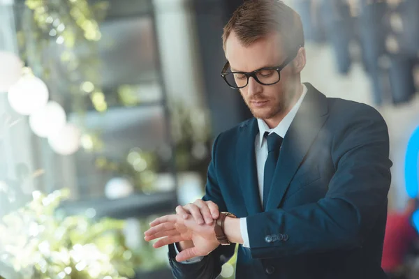 Portrait of confident businessman in eyeglasses checking time in cafe — Stock Photo