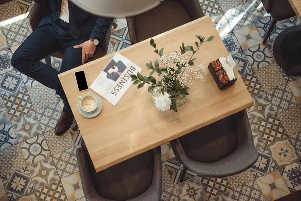 Vista aerea di uomo d'affari in giacca e cravatta a tavola con giornale, tazza di caffè e smartphone nel caffè — Foto stock