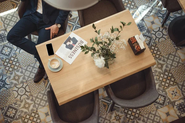 Overhead view of businessman in suit at table with newspaper, cup of coffee and smartphone in cafe — Stock Photo