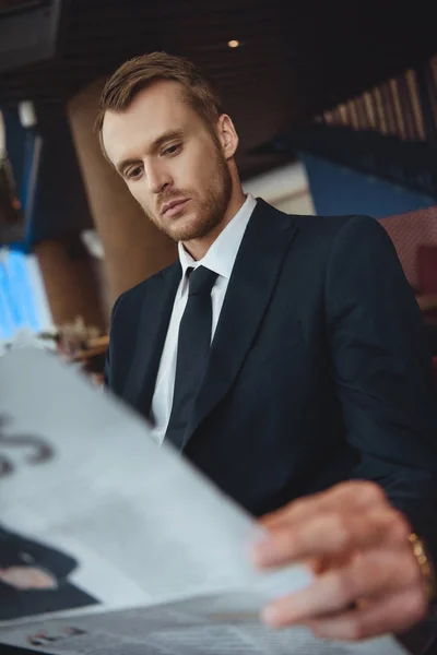 Concentrated businessman in black suit reading newspaper in cafe — Stock Photo