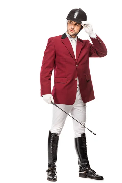 Handsome young horseman in uniform holding horseman stick and looking away isolated on white — Stock Photo